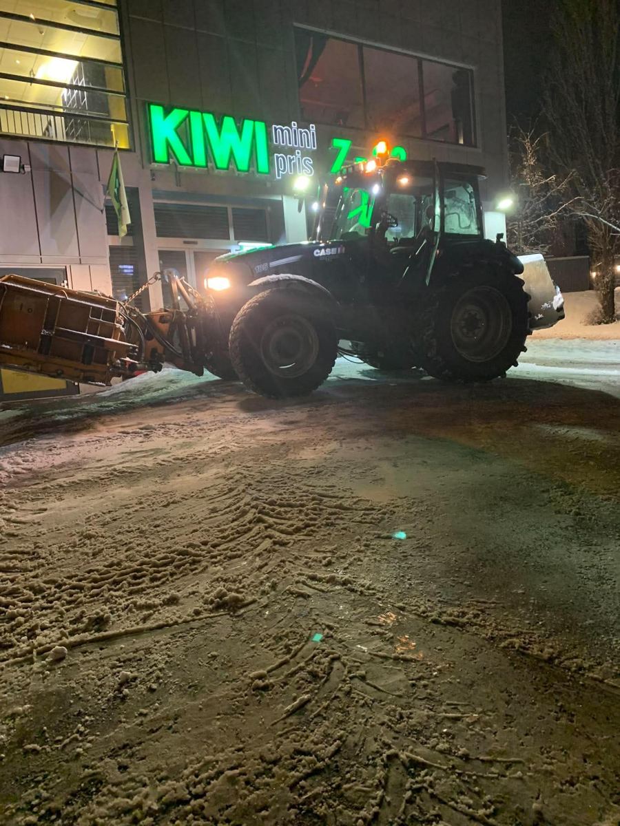 Traktor med brøyteskjær rydder snø utenfor butikk om natten